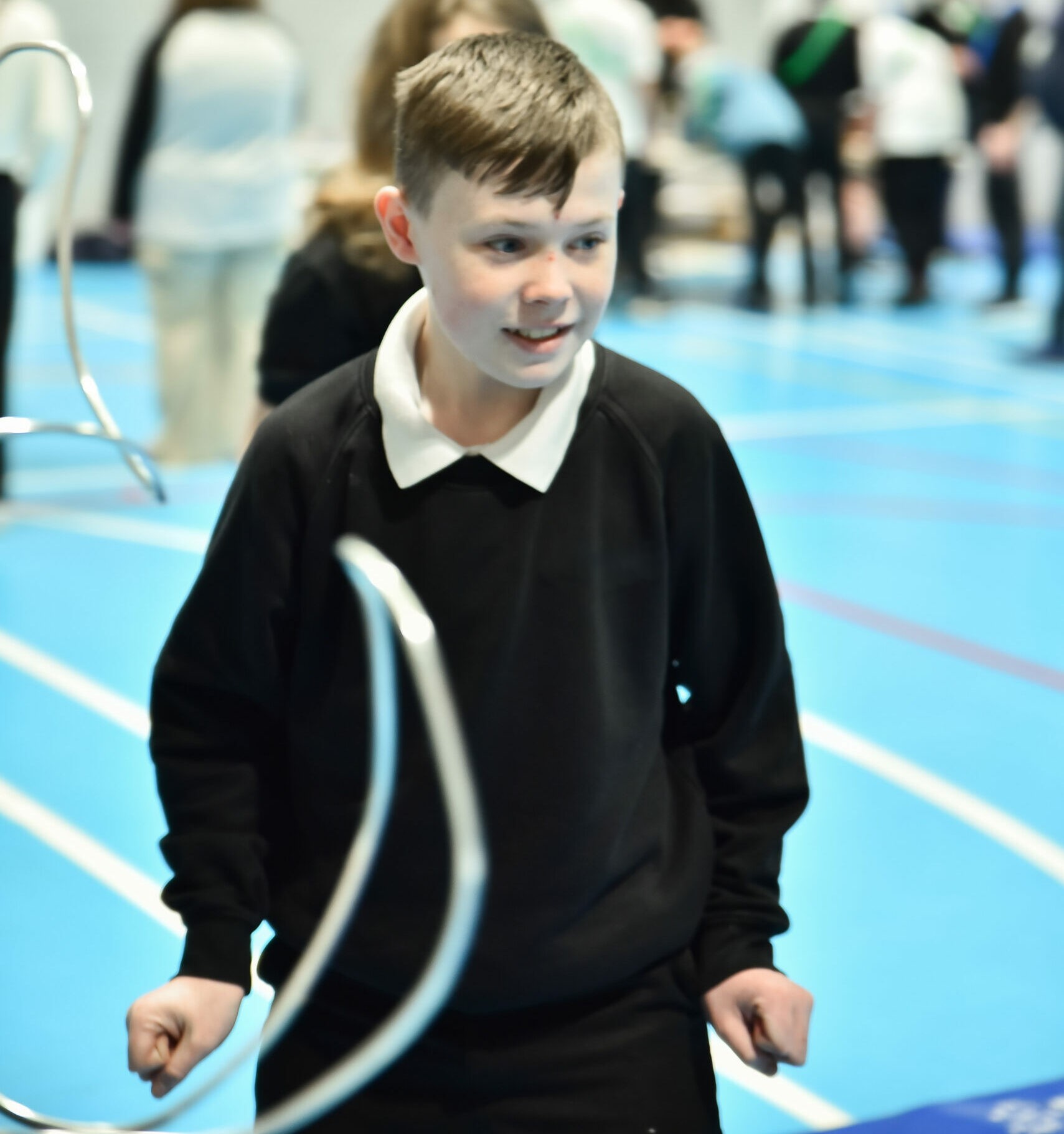 Pupil in school uniform standing in a sports hall with other students blurred in the background