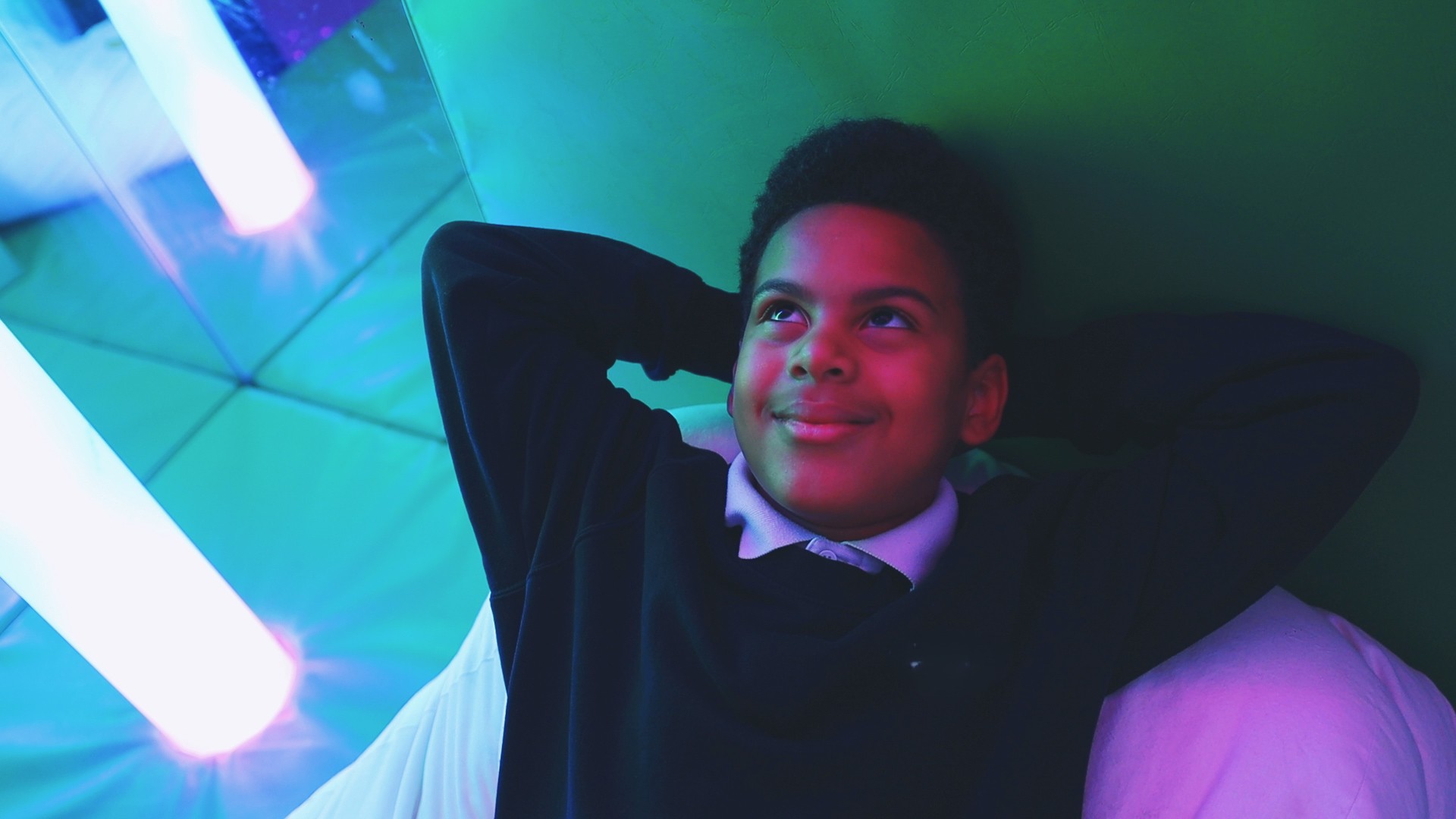 Pupil in school uniform relaxing on a beanbag under colourful lights