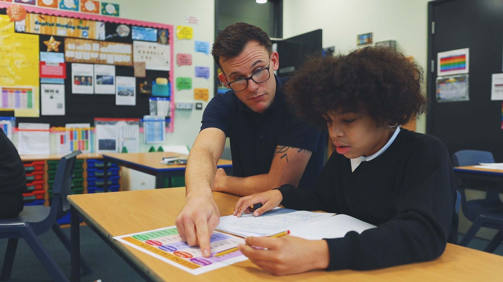 Teacher supporting a pupil with classroom work at a desk