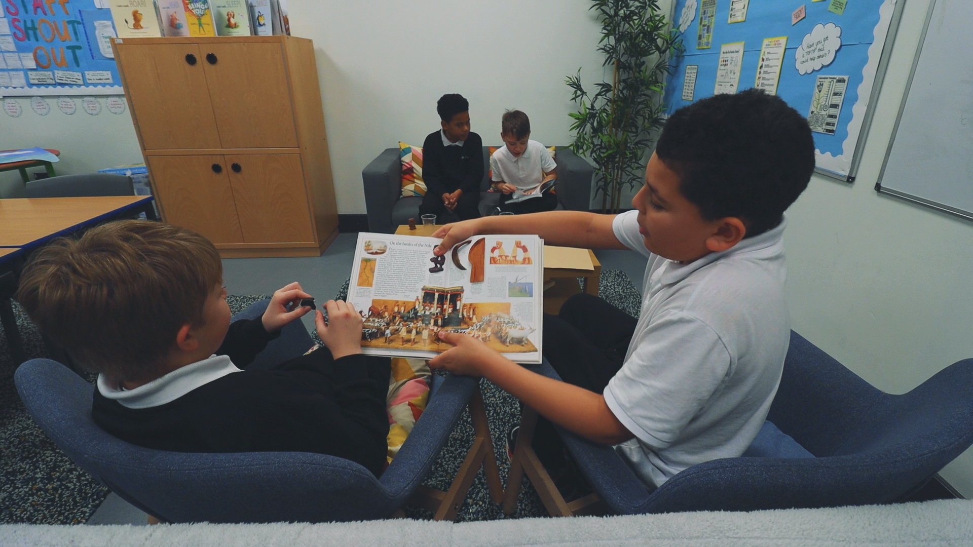 Pupils sitting together in a classroom, sharing and discussing a book